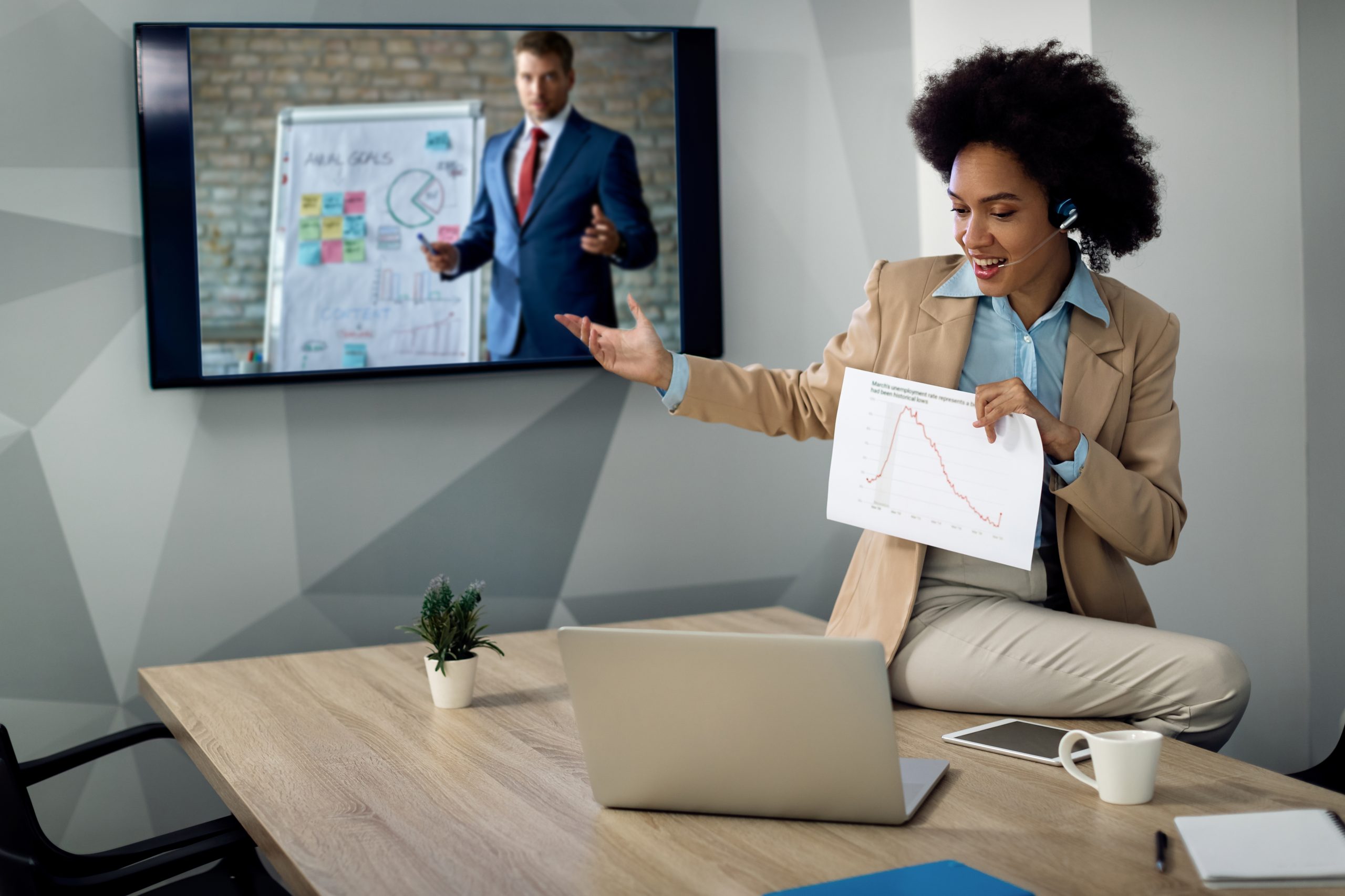 Happy black entrepreneur explaining business graph during conference call in the office.