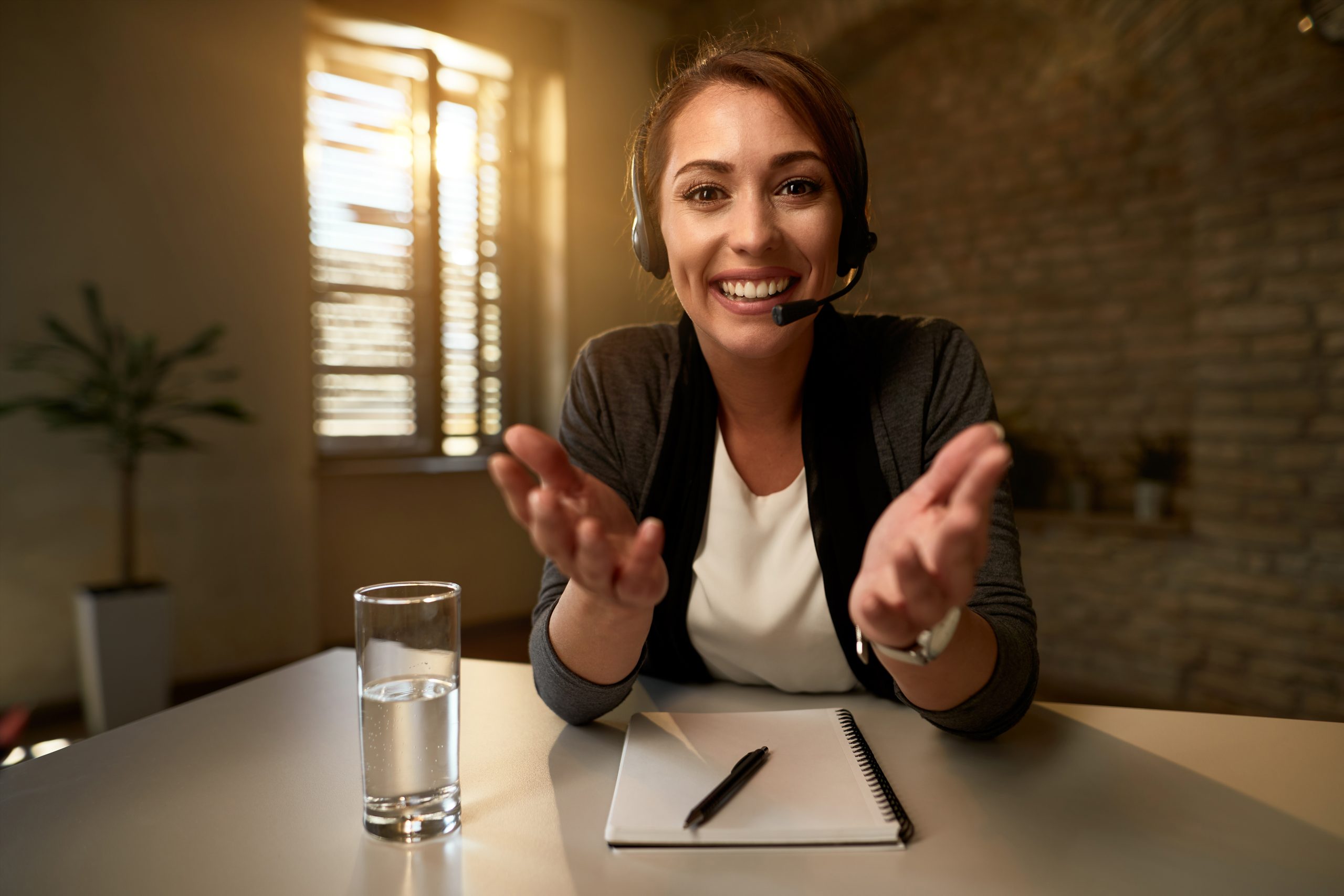 Happy call center agent with headset gesturing while looking at the camera.