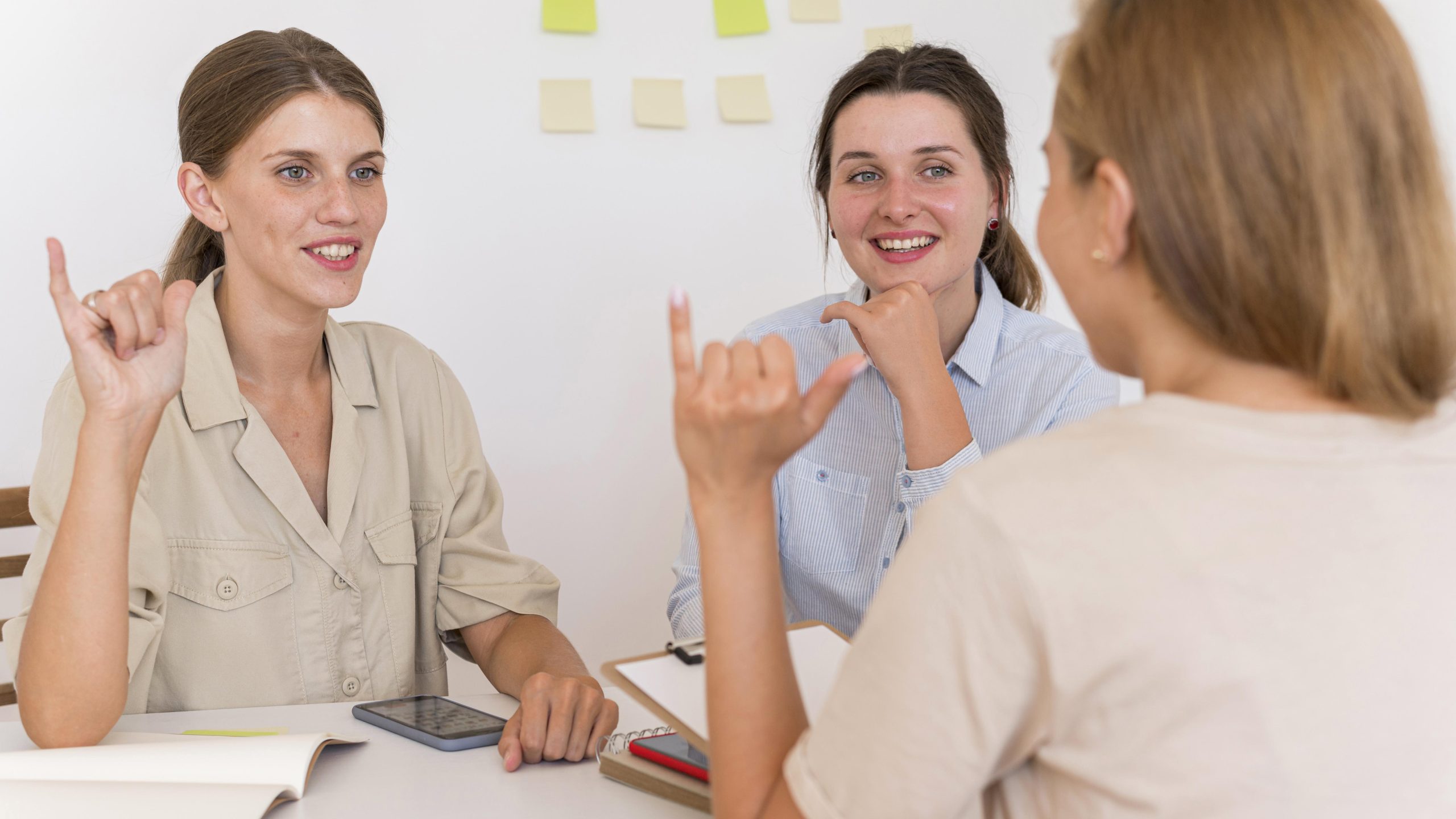 smiley women conversing around a table using sign language