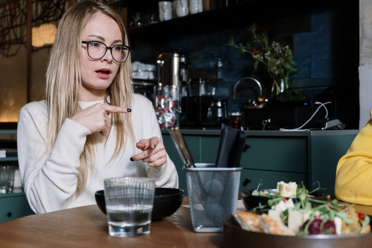 Woman in White Long Sleeve Shirt Signing to communicate with a friend at a restaurant.