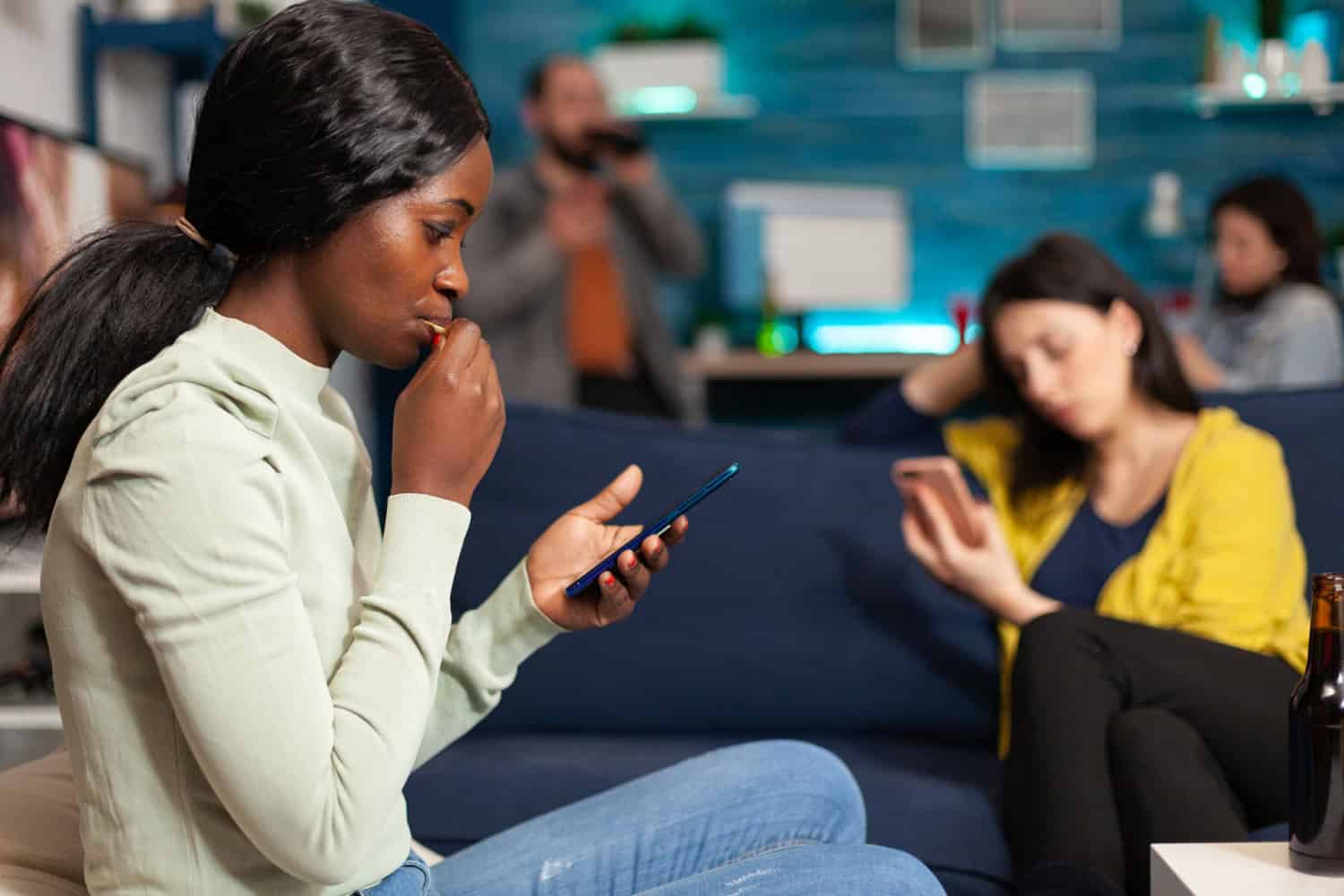 Multiracial friends relaxing on couch while surfing news on internet using mobile speding time together during surprise party. Group of multi-ethnic people watching online funny movie in living room.